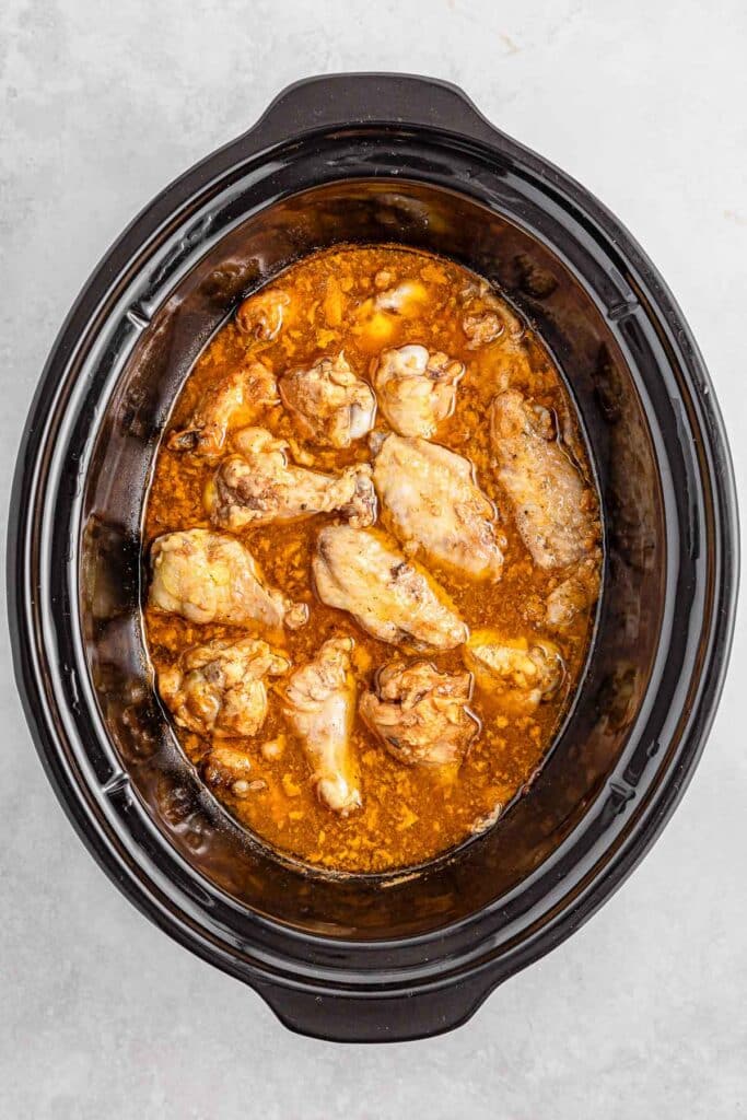 Chicken wings simmering in sauce inside a black slow cooker.