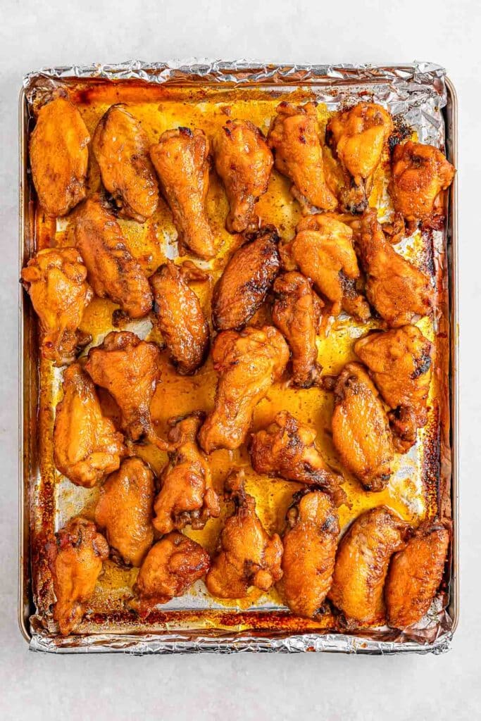 A baking sheet lined with foil holds several cooked hot honey chicken wings.