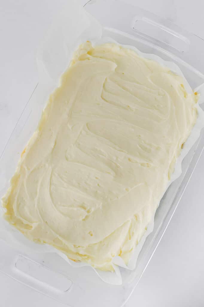 A clear rectangular dish filled with a smooth layer of cream cheese frosting spread evenly.