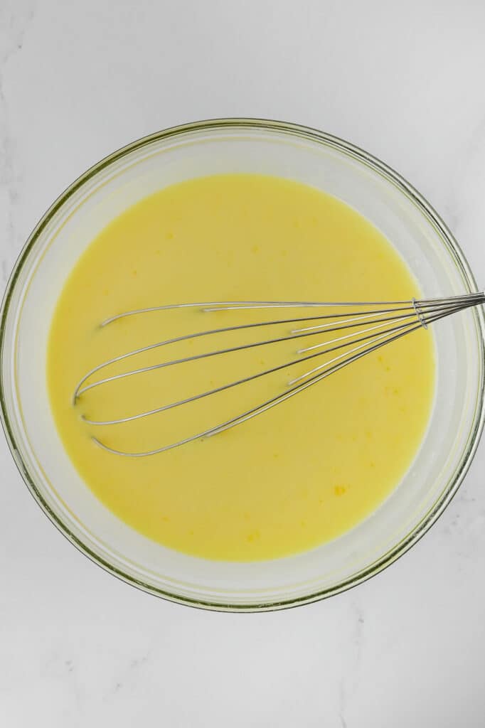 A glass bowl containing lemon pudding with a metal whisk on a white countertop.