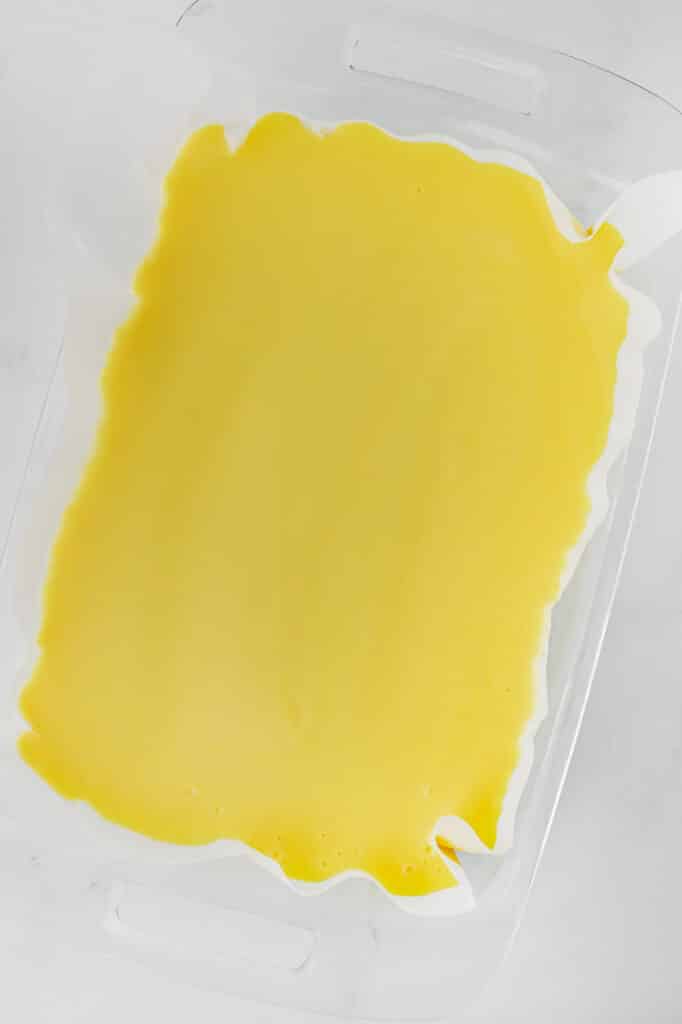 A rectangular glass baking dish filled with a smooth layer of lemon pudding spread over the crush and cream cheese layer.