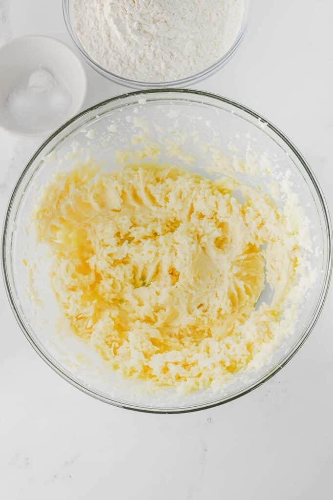 A glass bowl with creamed butter with an added egg, vanilla extract, lemon juice and lemon zest whisked together.