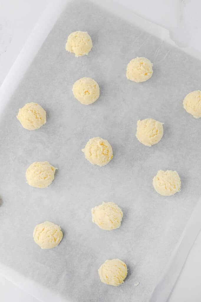 Balls of raw cookie dough are evenly spaced on a parchment-lined baking sheet, ready to be baked.