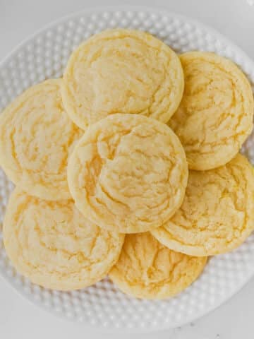 A white plate with seven round lemon sugar cookies on a white surface.