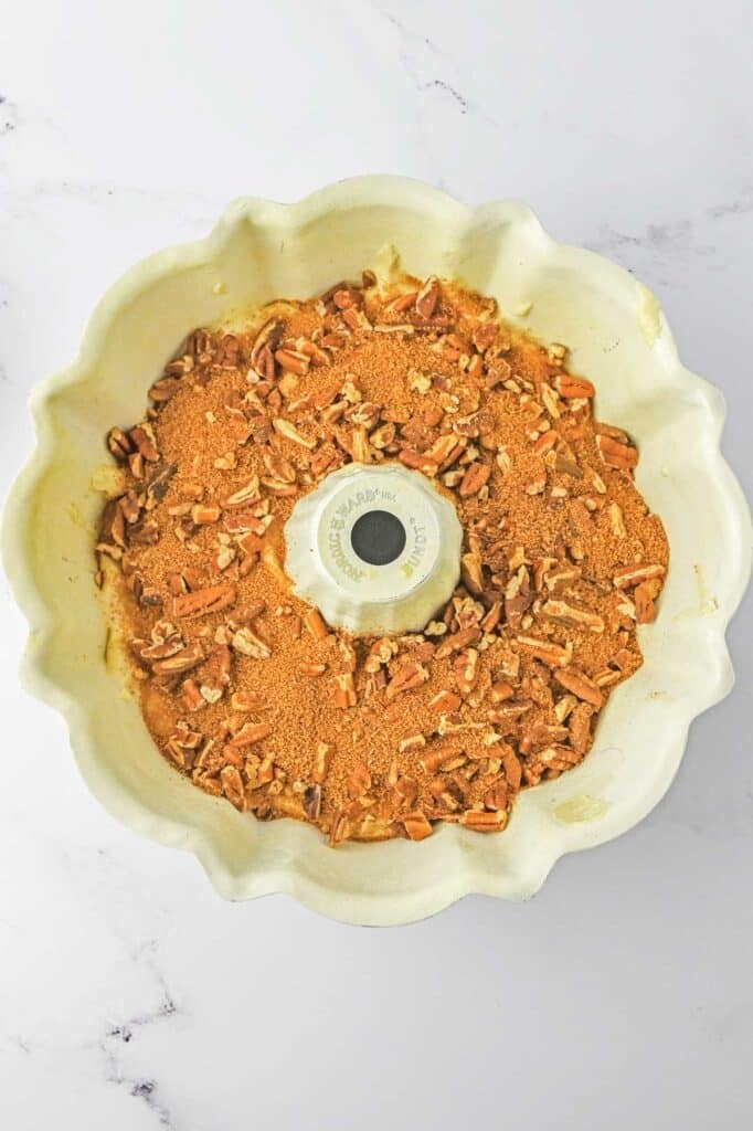 A bundt pan filled with cake batter filled with a layer of chopped pecans and brown sugar.