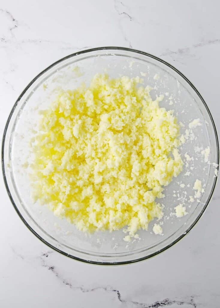 A glass bowl with butter and sugar added in being mixed togehter.
