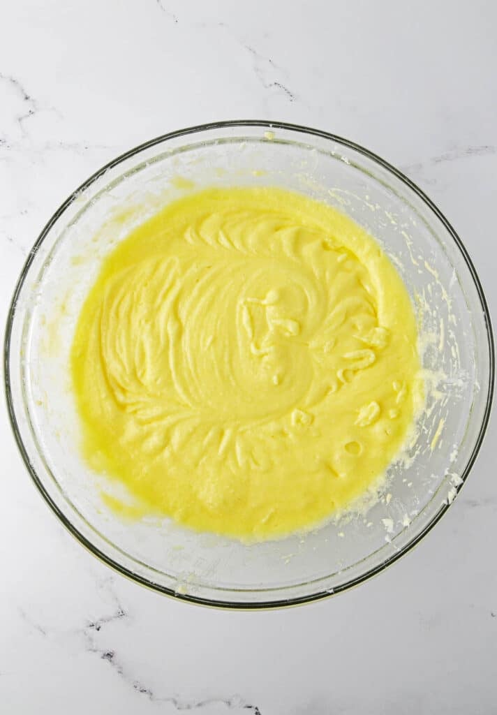 A glass mixing bowl filled with smooth, yellow cake batter.
