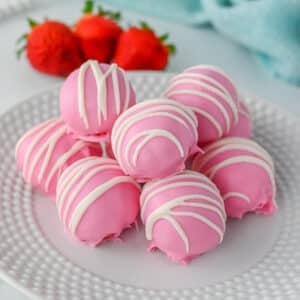 A plate of pink strawberry truffles drizzled with white icing, with strawberries in the background.