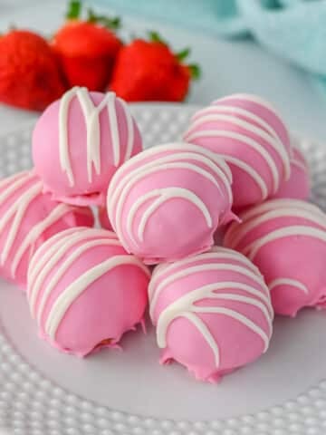 A plate of pink strawberry truffles drizzled with white icing, with strawberries in the background.