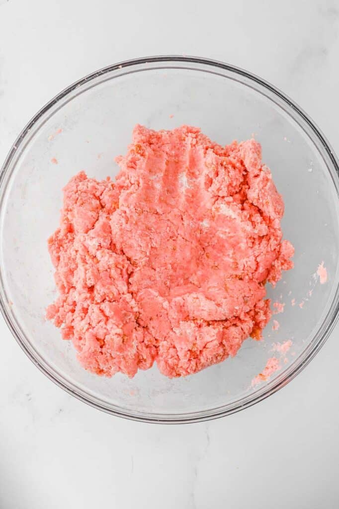 A glass bowl with crumpled strawberry cake mixed with cream cheese folded together.