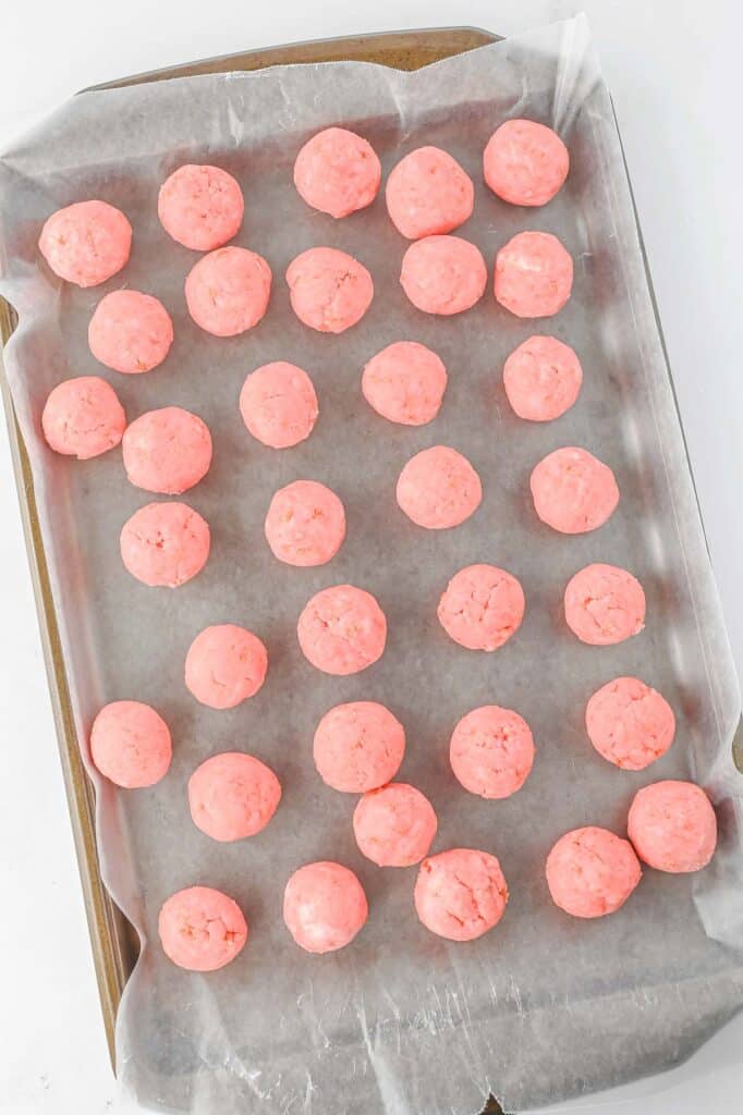 A baking sheet lined with parchment paper and topped with rows of evenly spaced strawberry cake balls.