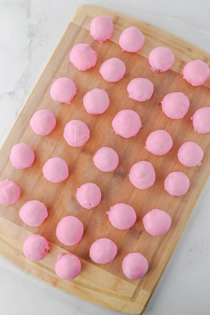 A wooden board holds neatly arranged strawberry cake balls covered with a pink candy melt icing.