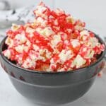 A black bowl filled with popcorn coated in bright red strawberry sauce.
