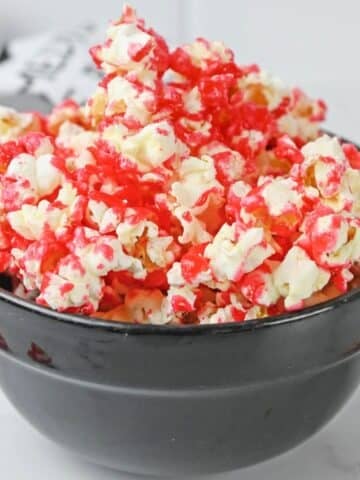 A black bowl filled with popcorn coated in bright red strawberry sauce.