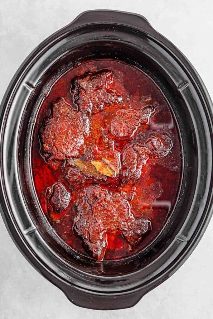 A slow cooker filled with meat in a rich, red sauce.