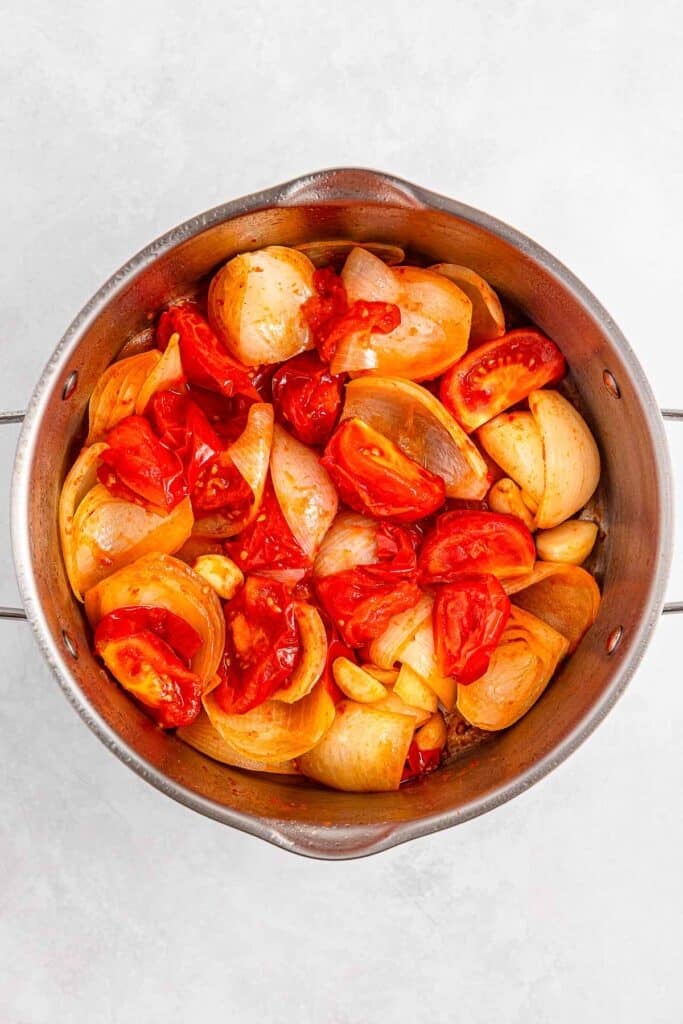 Tomatoes, onions, and garlic cloves sauteed in a large pot.