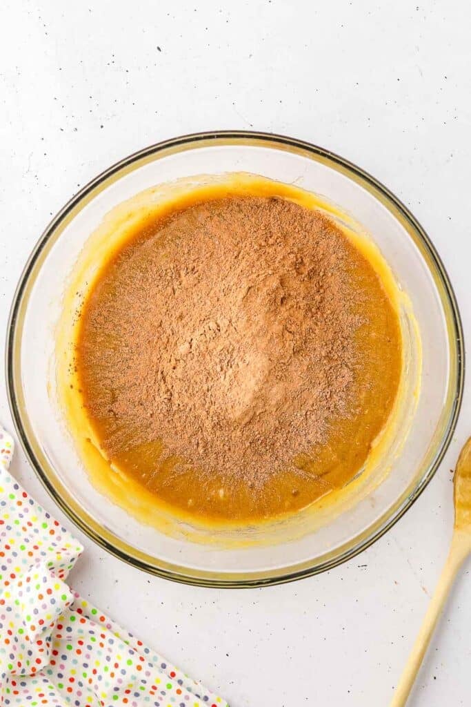 A glass bowl containing a yellow batter with cocoa powder mixture over top, ready to be mixed.