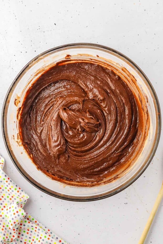 A glass bowl filled with smooth, swirled chocolate batter sits on a white surface.