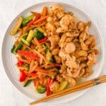 A white plate with hibachi chicken and a mix of sautéed vegetables including carrots, broccoli, zucchini, and red and orange bell pepper with chopsticks on the side.