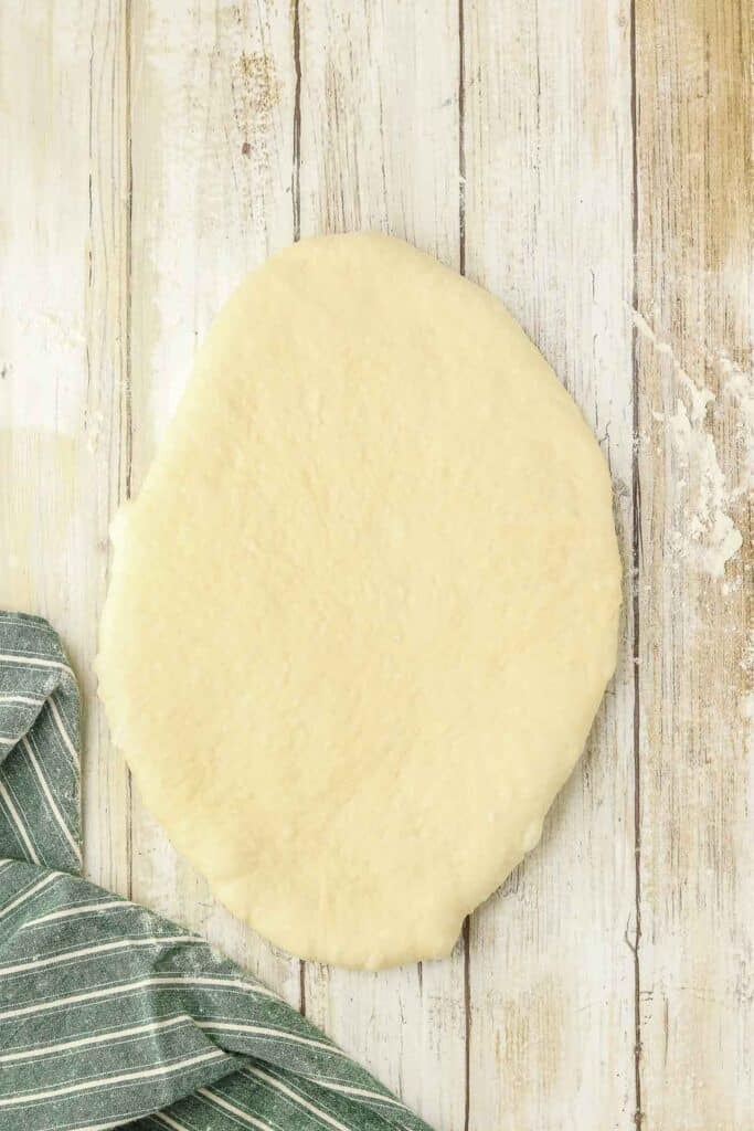 A ball of rolled-out dough in an oval shape on a wooden surface.