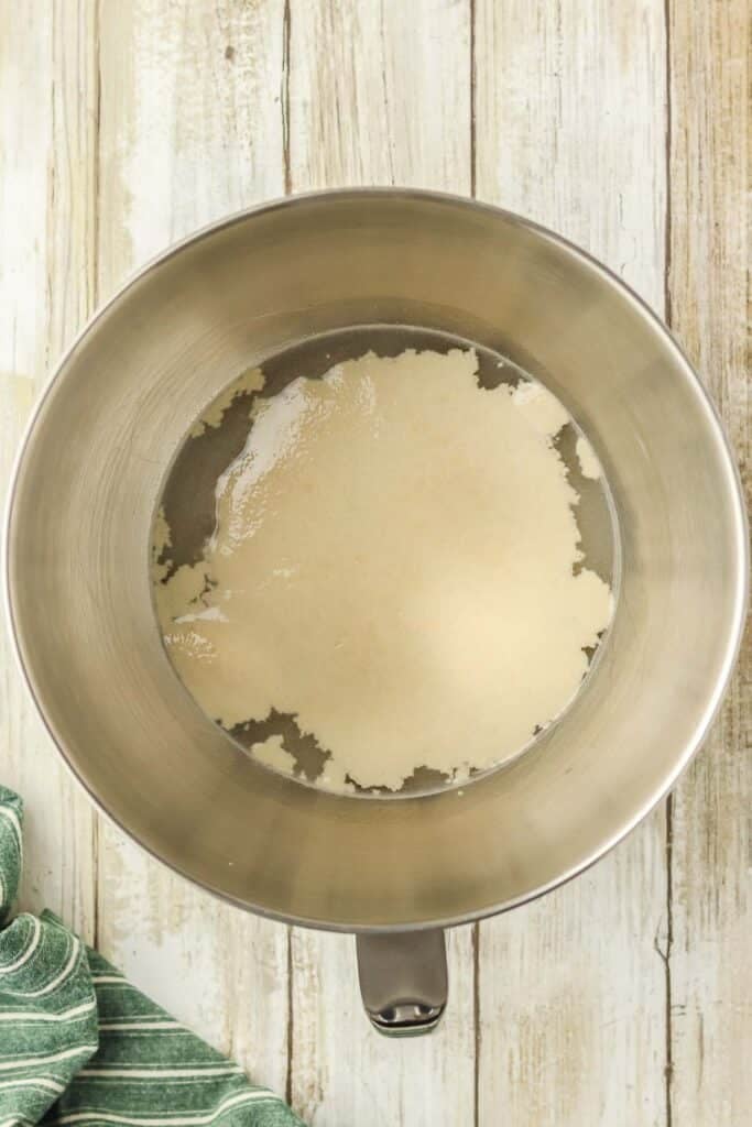 A metal mixing bowl containing a dissolved yeast mixture.