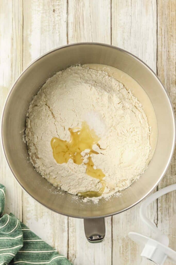 A metal mixing bowl contains flour, sea salt and a small amount of olive oil on top to be mixed into the yeast mixture.