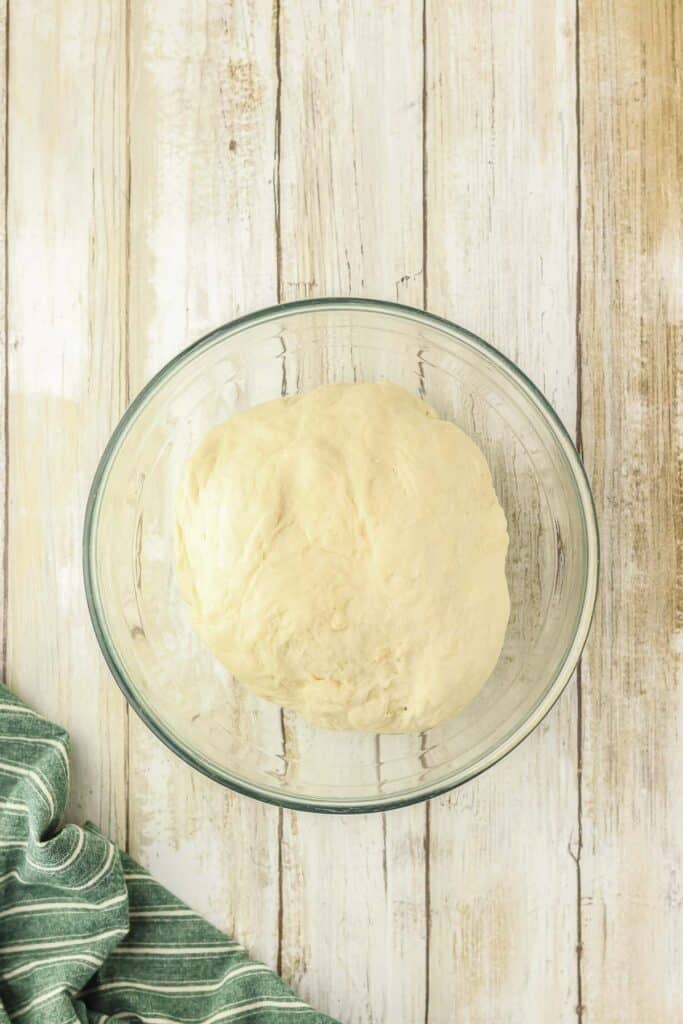 A ball of dough sits in a clear glass bowl.