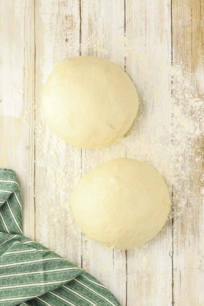 Two balls of raw dough rest on a floured wooden surface.