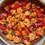 A skillet filled with cooked thai shrimp, red bell peppers, pineapple chunks, and chopped green onions in a glossy sauce.