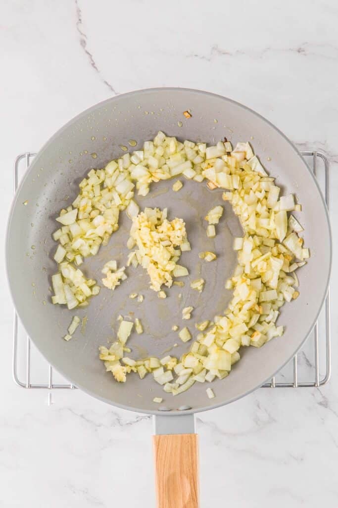 Chopped onions and minced garlic sautéing in a light-colored frying pan.