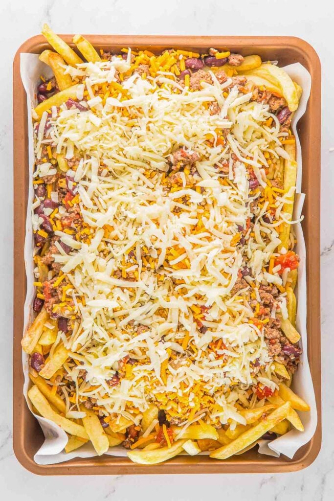A baking sheet filled with French fries topped with ground meat, beans, diced vegetables, and shredded cheese.