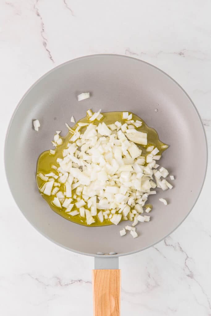 Chopped onions in a frying pan with oil, ready to be sautéed.