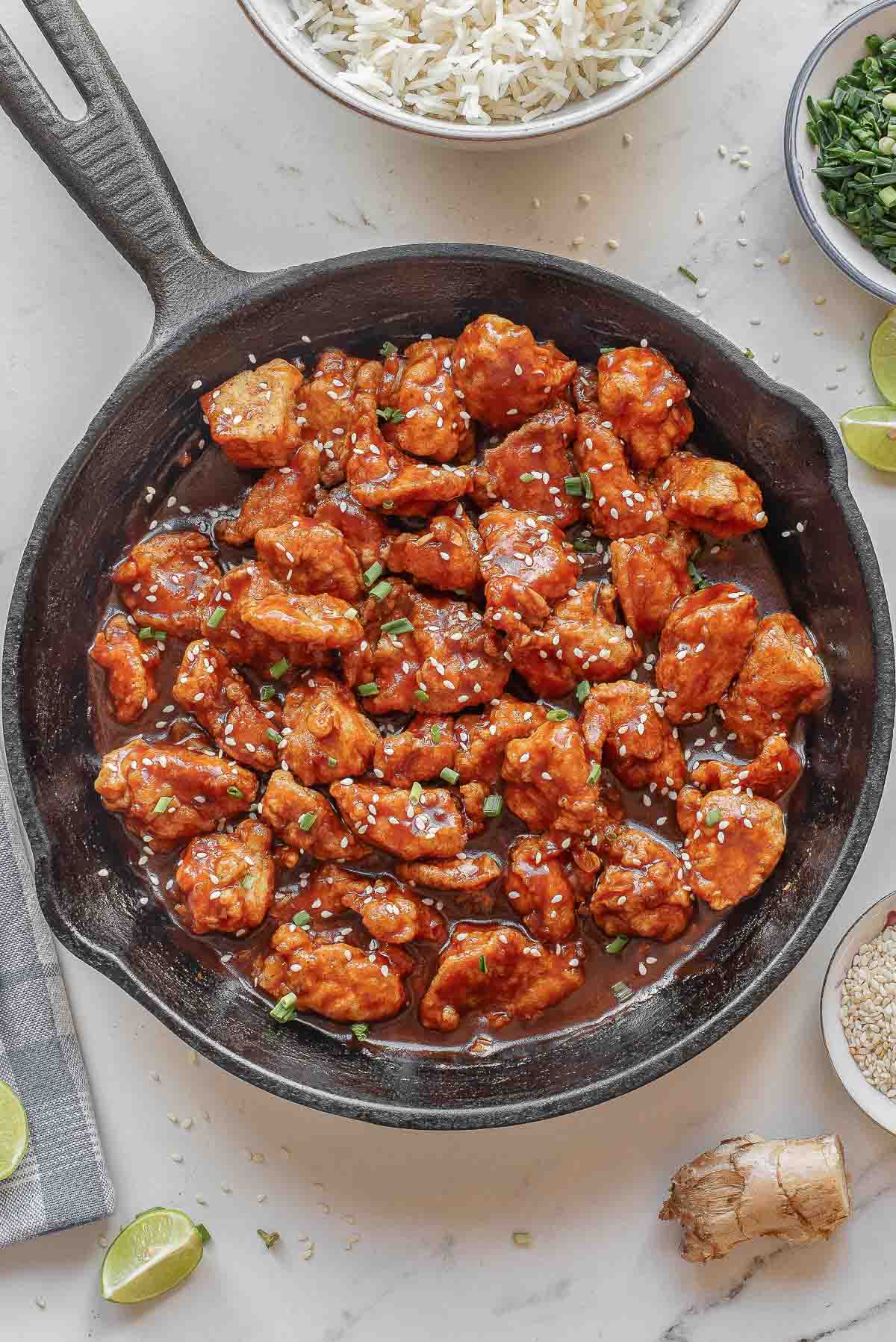 A cast iron skillet filled with empress chicken garnished with chopped green onions and sesame seeds.
