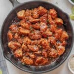 A cast iron skillet filled with empress chicken garnished with chopped green onions and sesame seeds.