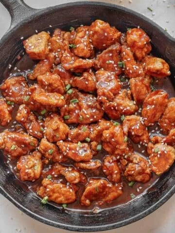 A cast iron skillet filled with empress chicken garnished with chopped green onions and sesame seeds.