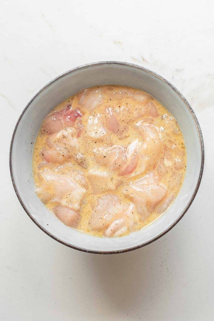 sliced chicken breast in a bowl with egg, cornstarch, salt, and pepper.