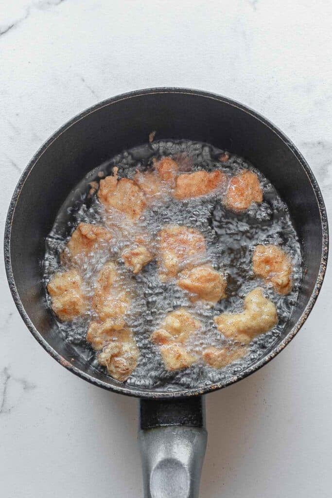 Small pieces of chicken are being fried in hot oil inside a black pan.