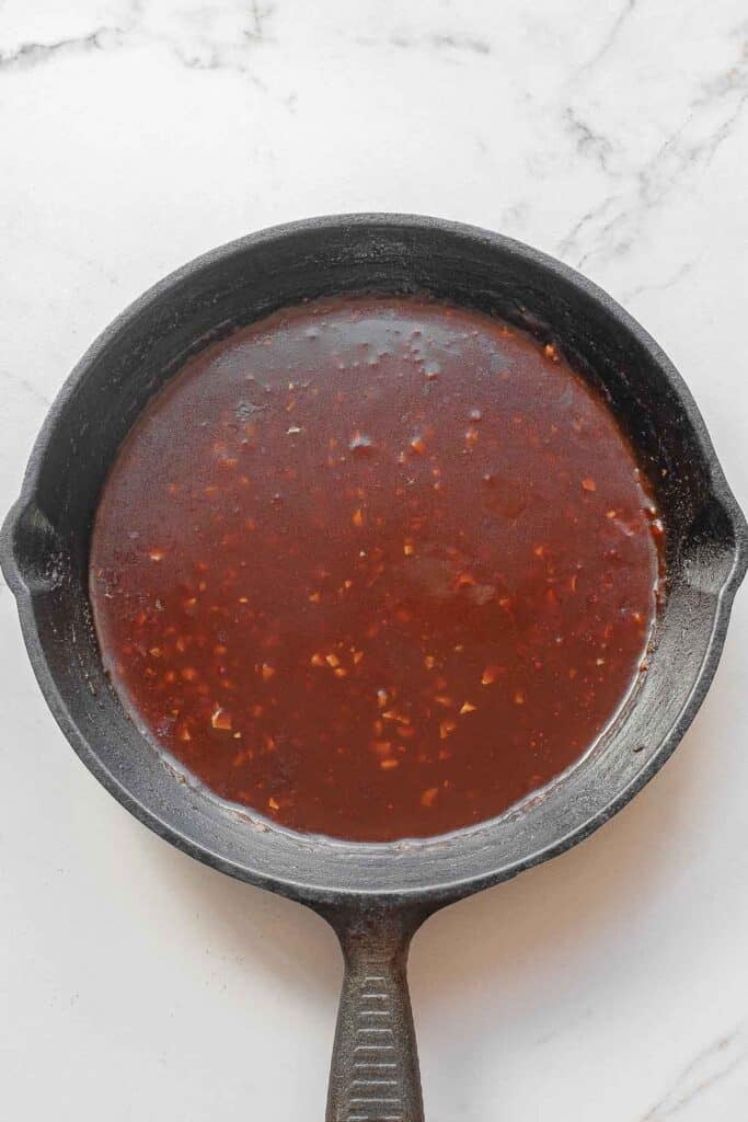 A cast iron skillet filled sauce mixture with sautéed garlic and ginger added in.