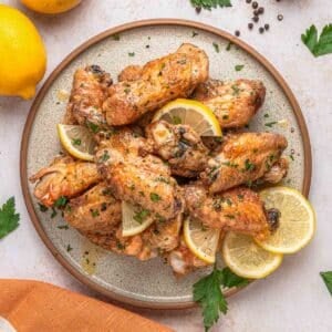 A plate of baked lemon pepper chicken wings garnished with lemon slices and chopped herbs.