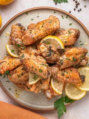 A plate of baked lemon pepper chicken wings garnished with lemon slices and chopped herbs.