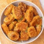 A white bowl filled with sweet potato tater tots garnished with chopped herbs on a wooden cutting board.