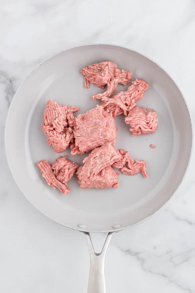Raw ground turkey sits in a white frying pan on a marble countertop.