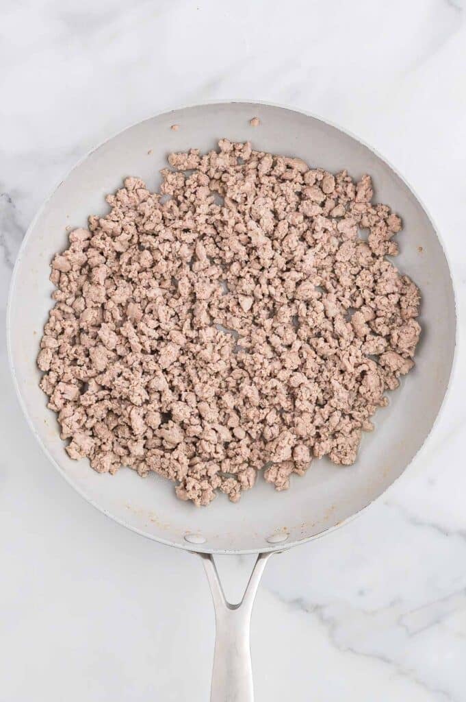 Cooked ground turkey in a white skillet on a marble countertop.