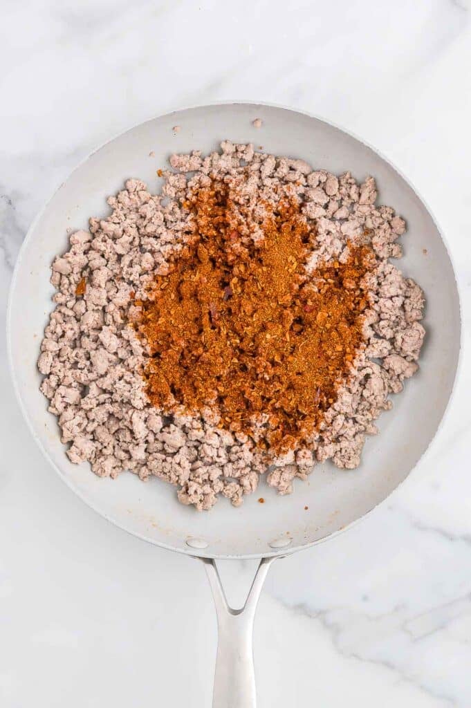 Ground turkey cooking in a white skillet with a mound of taco seasoning in the center.