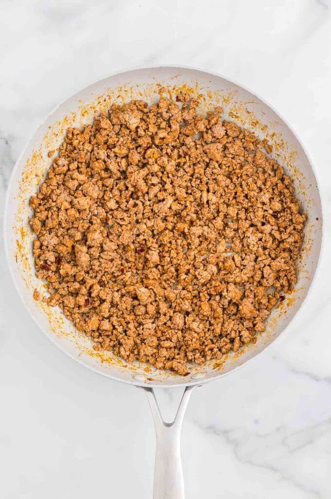 A white skillet filled with cooked, seasoned ground turkey on a marble surface.
