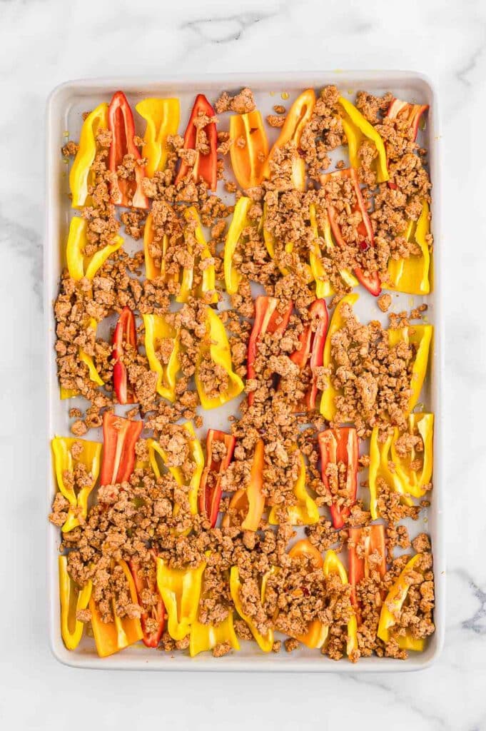 A baking sheet with halved yellow and red mini bell peppers topped with seasoned ground turkey, ready to be baked.