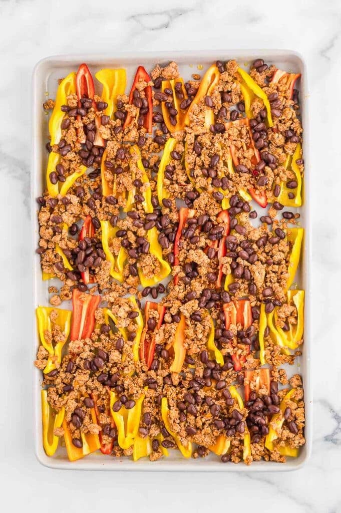 Sheet pan with halved yellow, red, and orange bell peppers topped with ground turkey and black beans.