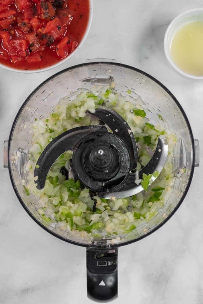 Chopped onions, garlic and green peppers in a food processor bowl.