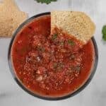 A tortilla chip dipped into a bowl of chunky red salsa.