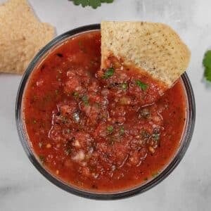 A tortilla chip dipped into a bowl of chunky red salsa.